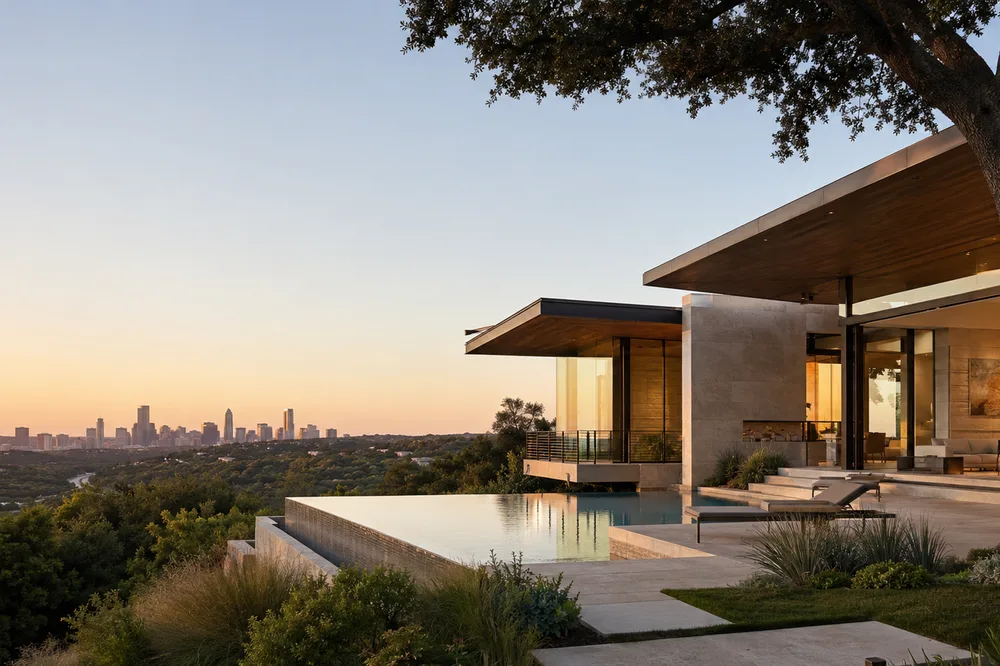 Contemporary hillside residence with deep roof overhangs, stone walls, an infinity pool, mature trees, and distant Austin views